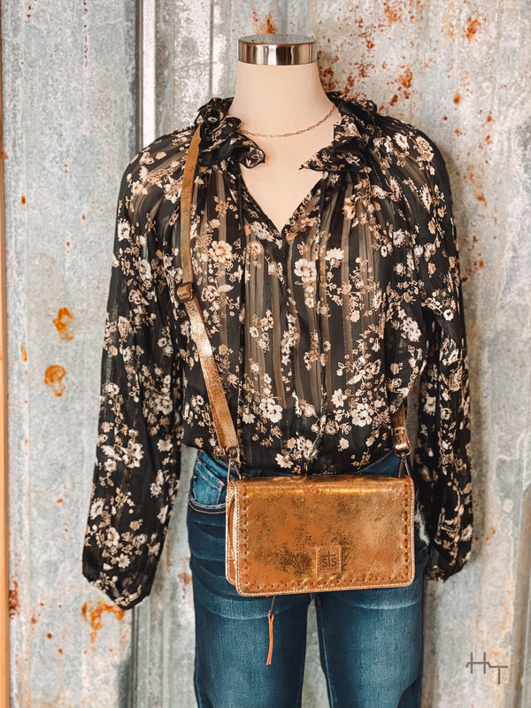 Photo of black and gold floral print blouse on mannequin with metallic gold crossbody purse with tin background